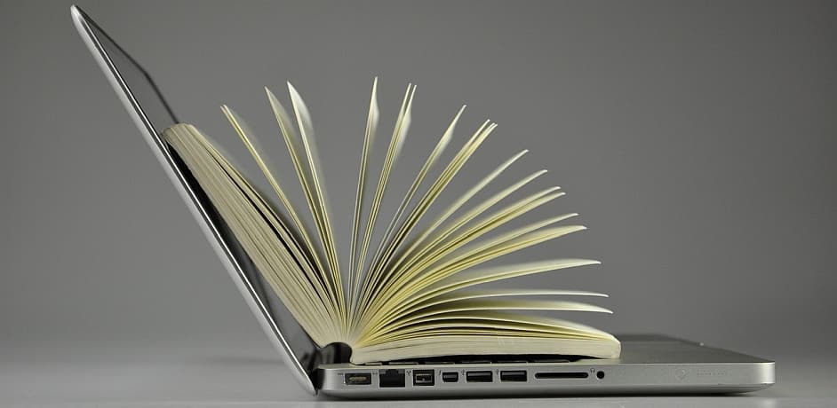 Bild eines offenen Laptops mit einem aufgeschlagenen Buch